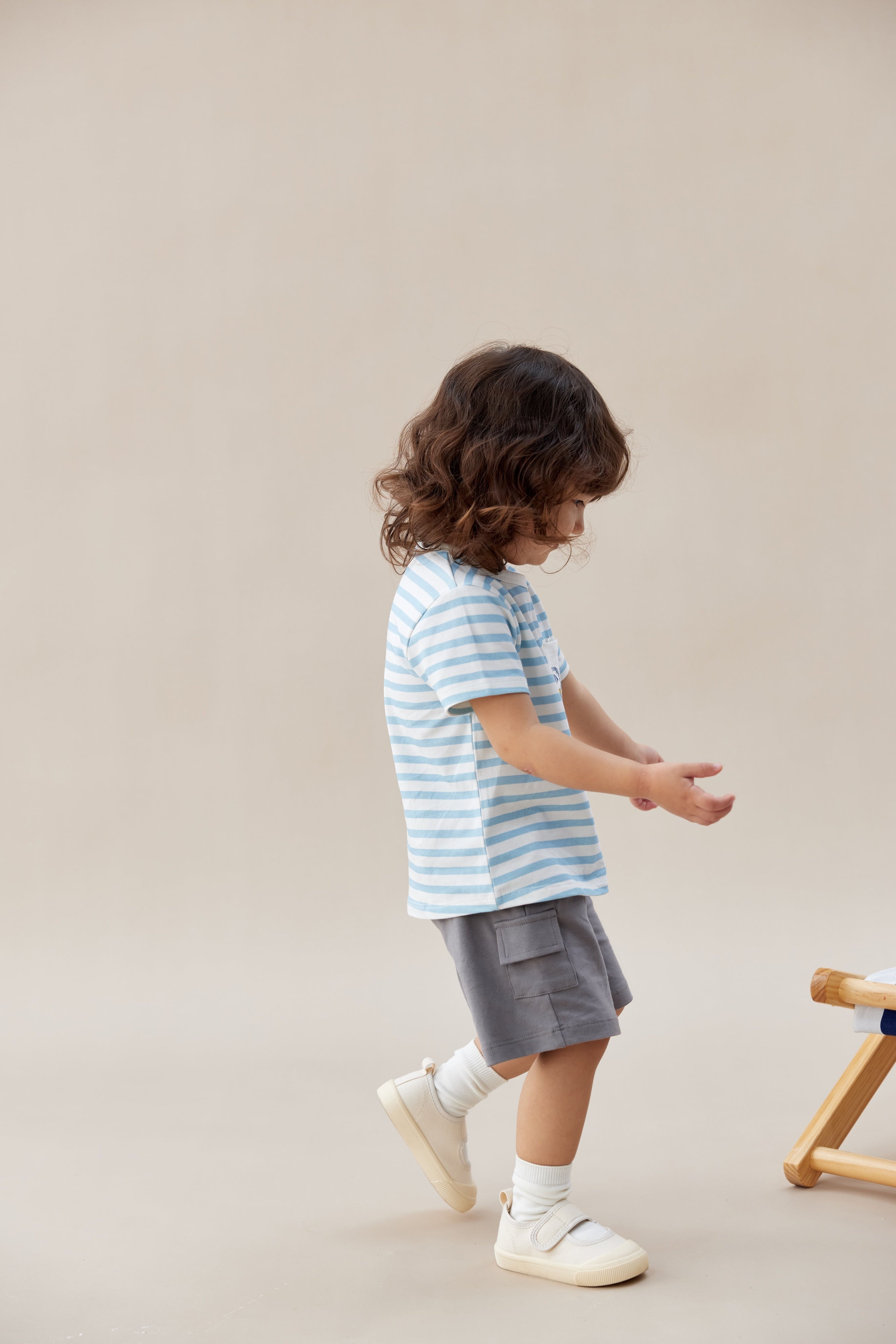 Child wearing a striped shirt and shorts standing on a beige background