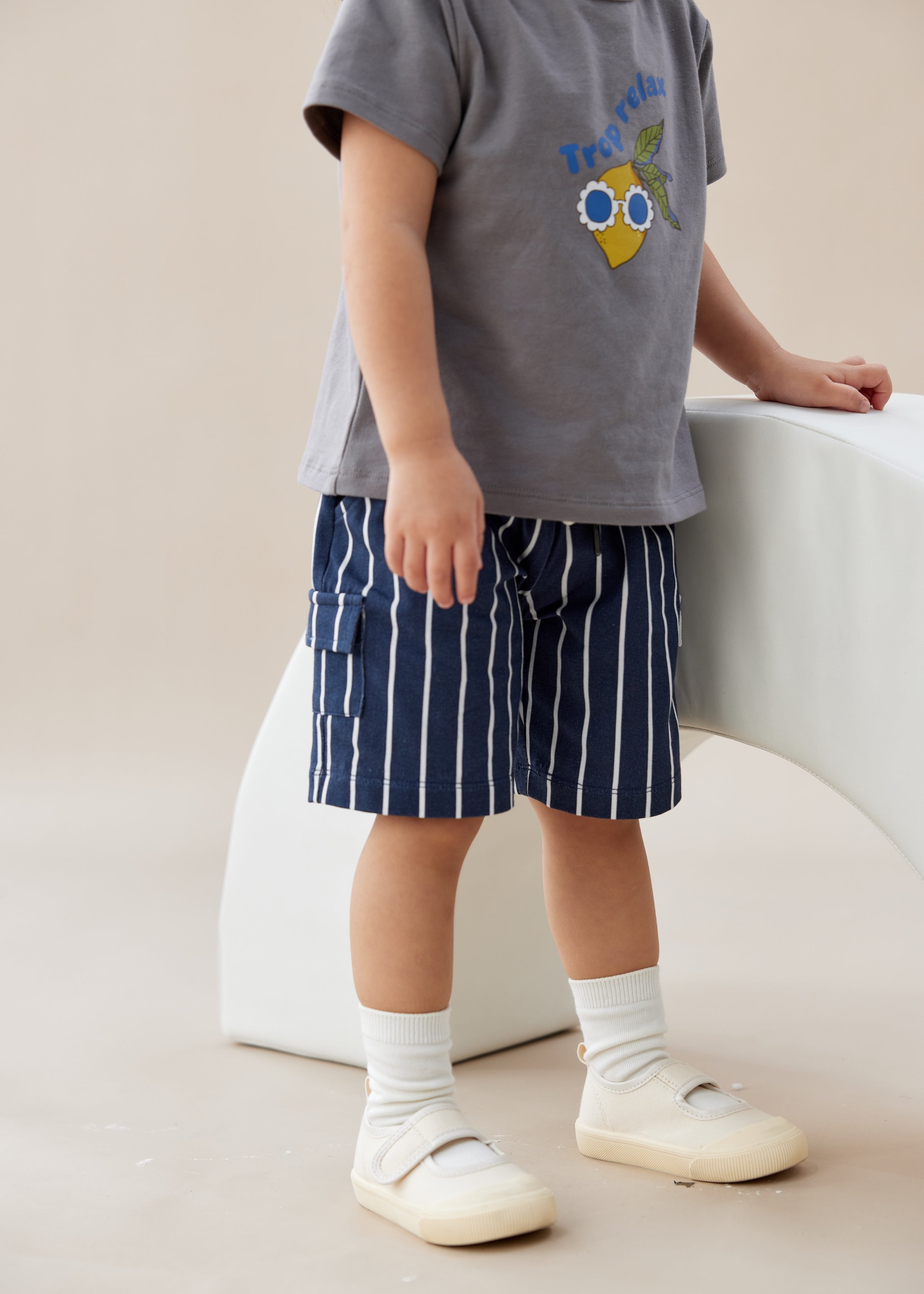 Child wearing a gray t-shirt with a graphic design and blue striped shorts, standing on a light-colored floor.