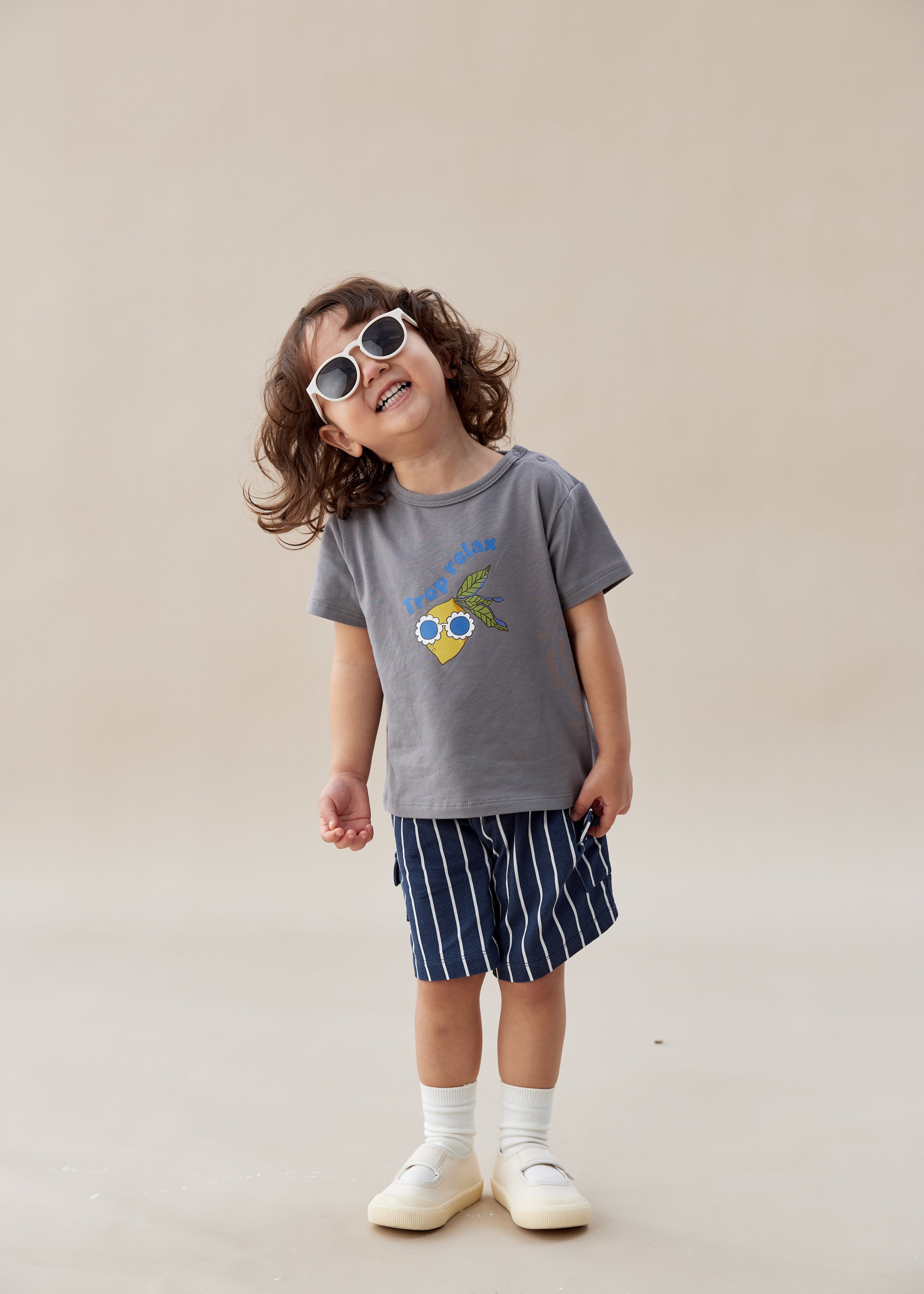 Child wearing a gray t-shirt with a graphic design and striped shorts on a beige background