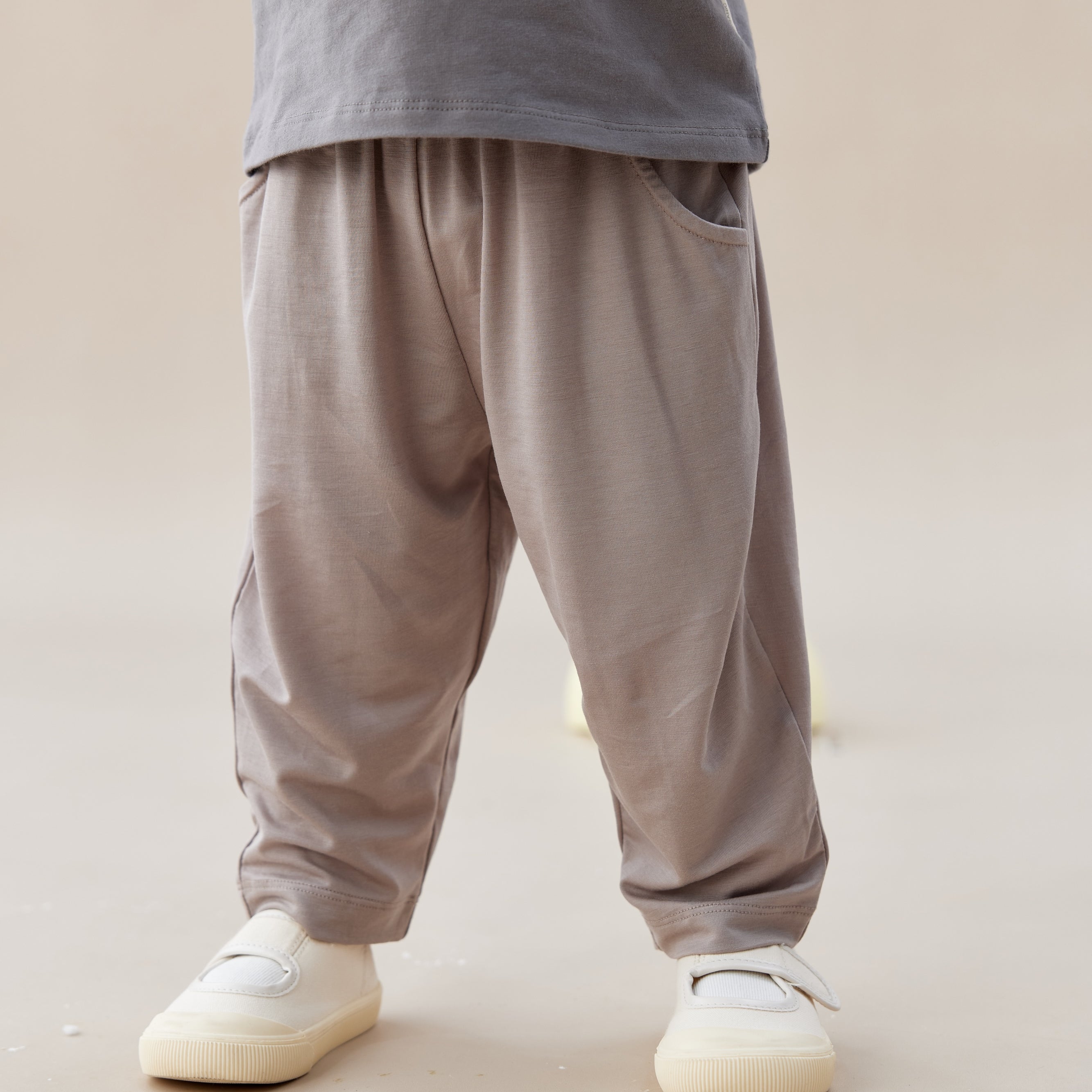 Person wearing gray pants and white shoes on a plain background