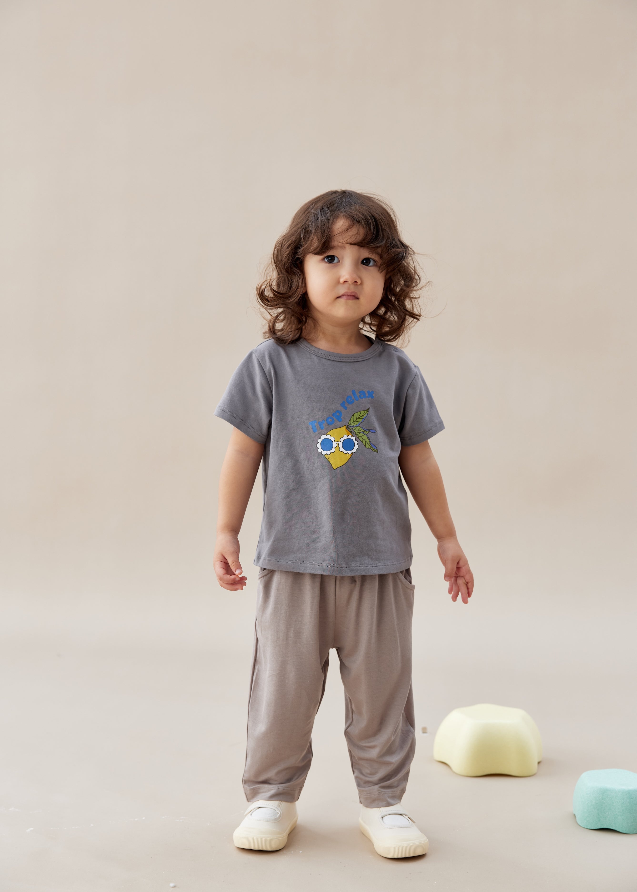 Child wearing a gray t-shirt with a colorful design and beige pants on a plain background