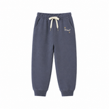 A pair of dark slate blue jogger sweatpants with a cream-colored drawstring and small gold embroidered text on the left thigh, displayed against a solid white background.