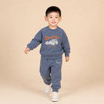 Child wearing a blue sweatshirt and pants with a 'Speed Time' graphic on a beige background