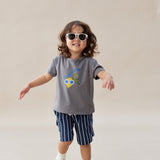 Child wearing a gray t-shirt with a colorful design and striped shorts on a plain background