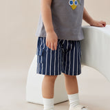 Child wearing a gray t-shirt with a graphic design and blue navy striped shorts, standing on a light-colored floor.