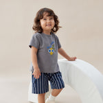 Child wearing a gray t-shirt with a colorful design and blue shorts, standing on a light-colored floor.