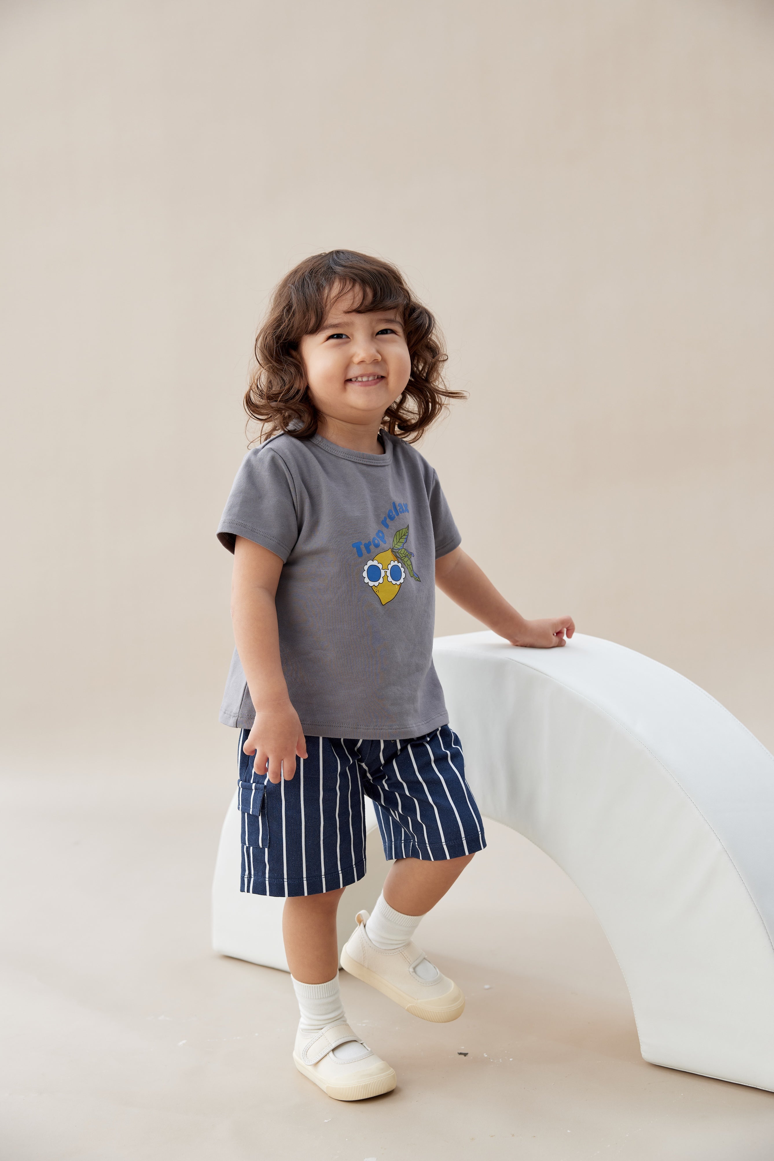 Child wearing a gray t-shirt with a colorful design and blue shorts, standing on a light-colored floor.