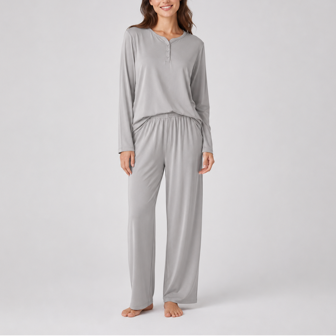 A woman modeling a light gray two-piece loungewear set consisting of a long-sleeve henley top and matching wide-leg pants, photographed against a neutral light gray studio background.