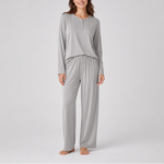 A woman modeling a light gray two-piece loungewear set consisting of a long-sleeve henley top and matching wide-leg pants, photographed against a neutral light gray studio background.