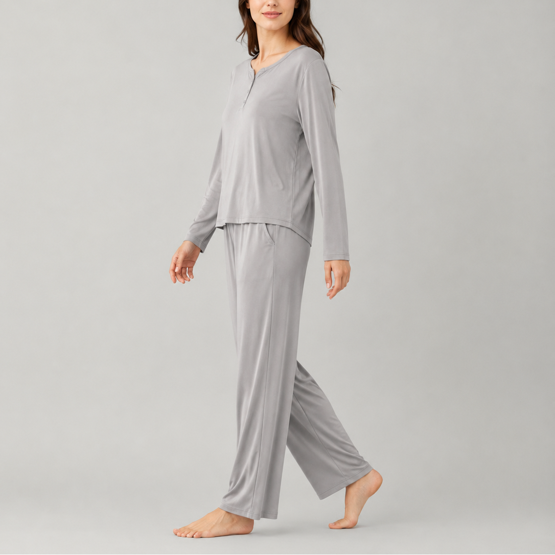 A woman modeling a light gray two-piece pajama set consisting of a long-sleeve henley top and matching wide-leg pants, photographed against a solid light gray studio background.