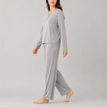 A woman modeling a light gray two-piece pajama set consisting of a long-sleeve henley top and matching wide-leg pants, photographed against a solid light gray studio background.