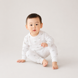 Baby wearing a white outfit with small patterns on a light gray background