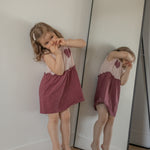 Young girl in a pink dress standing next to a mirror reflection.