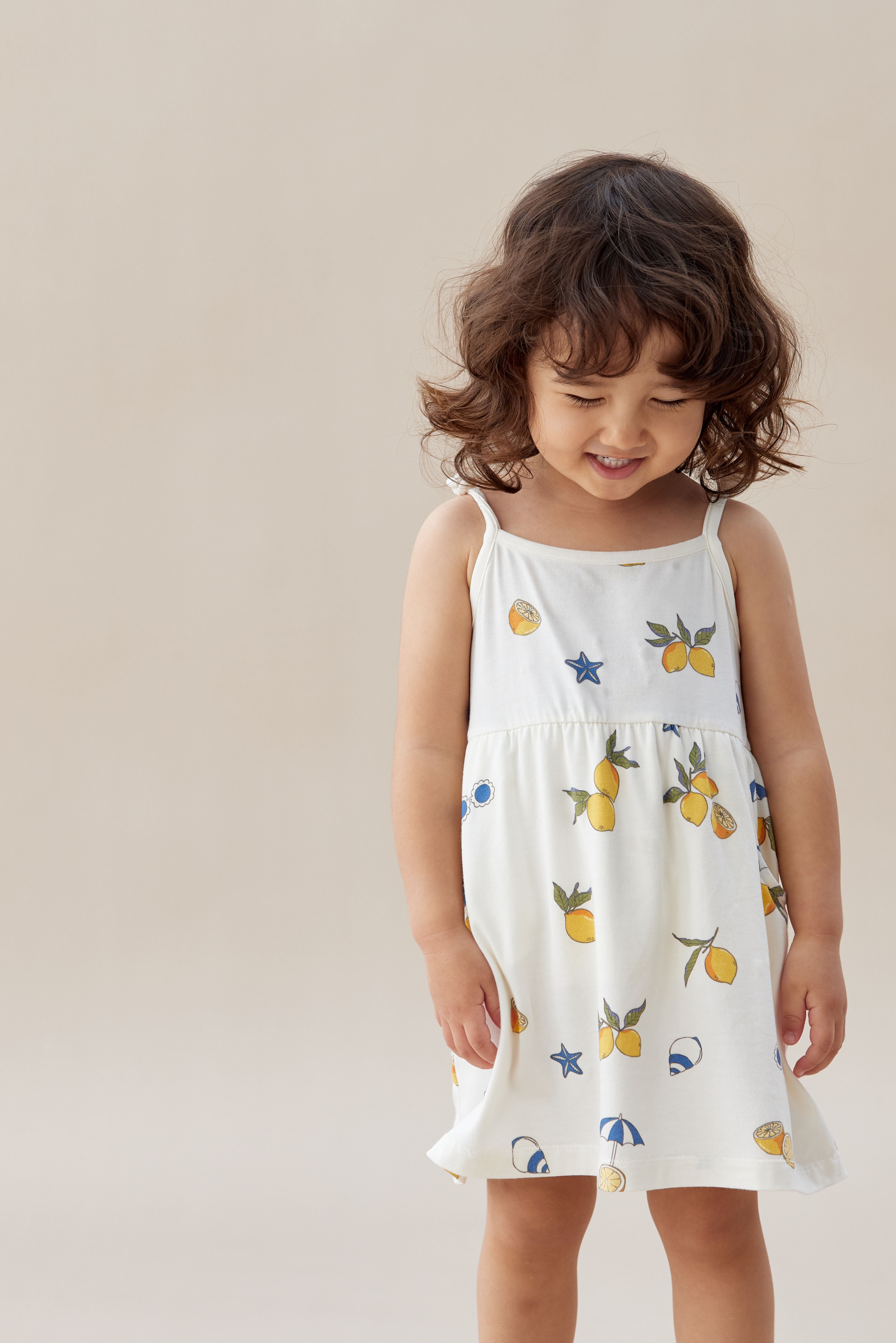baby gril wearing norsu organic organic toddler lemon dress and looking down to the ground