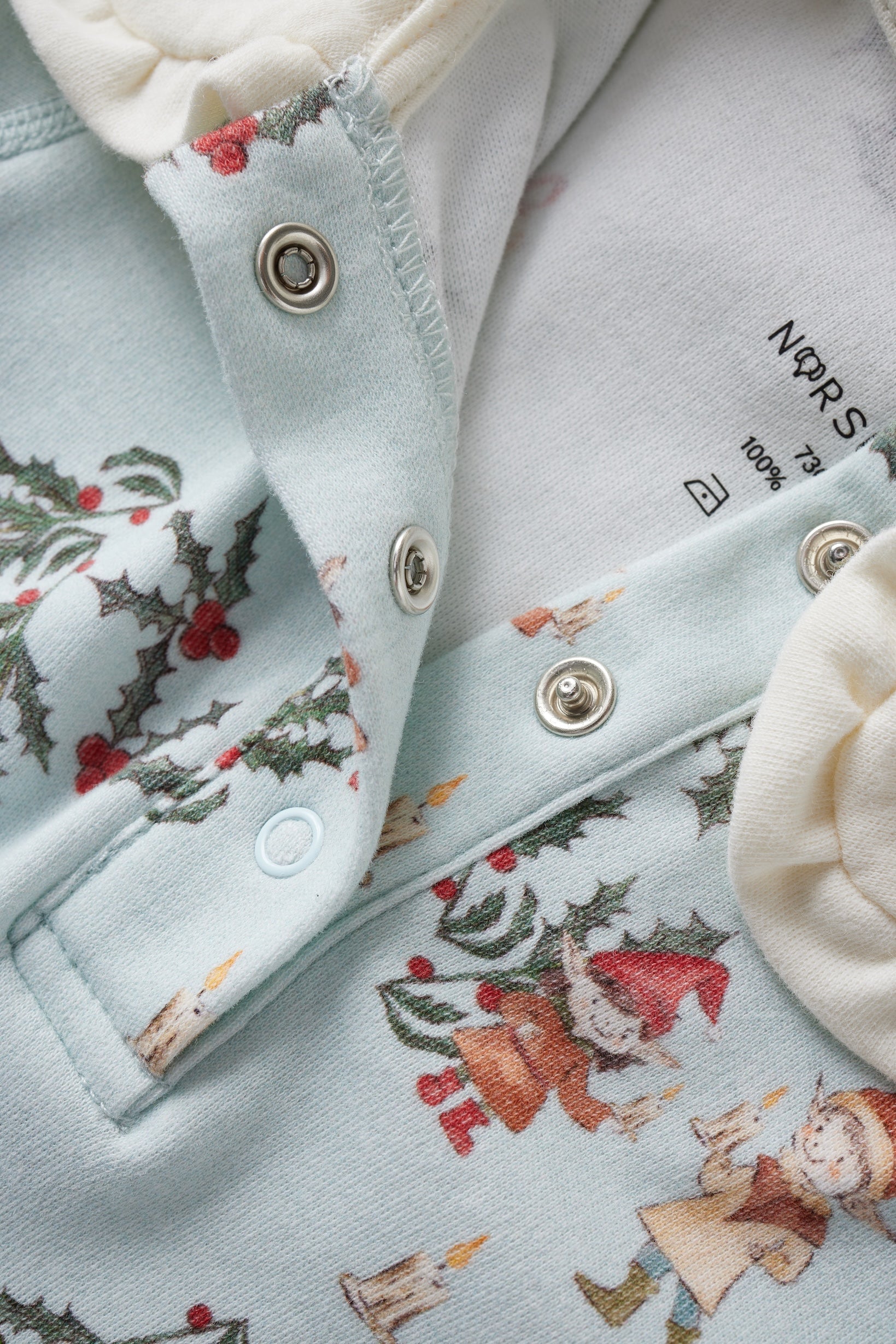 Close-up of a light blue fabric with Christmas-themed embroidery and buttons.