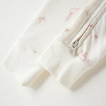 Close-up of a cream-colored fabric garment with a silver zipper and delicate pink bow patterns, set against a clean white background.