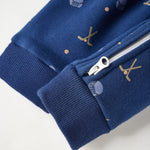 Close-up of a navy blue zippered garment, likely a baby jacket or sweatshirt, featuring ribbed cuffs and a small gold and white pattern on the fabric.