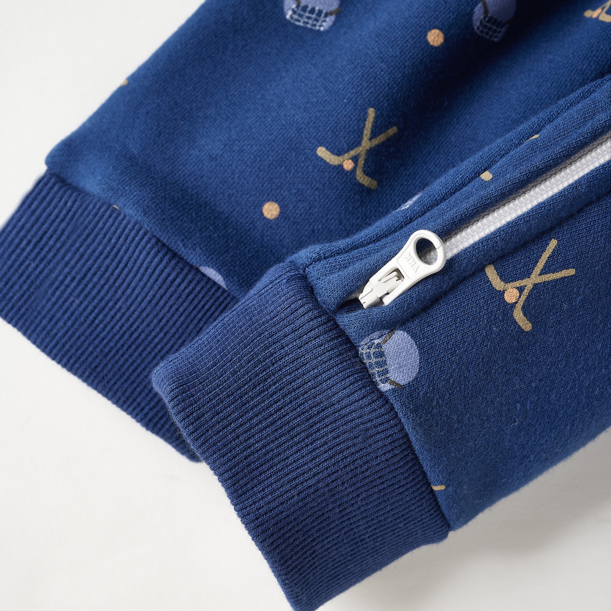 Close-up of a navy blue zippered garment, likely a baby jacket or sweatshirt, featuring ribbed cuffs and a small gold and white pattern on the fabric.