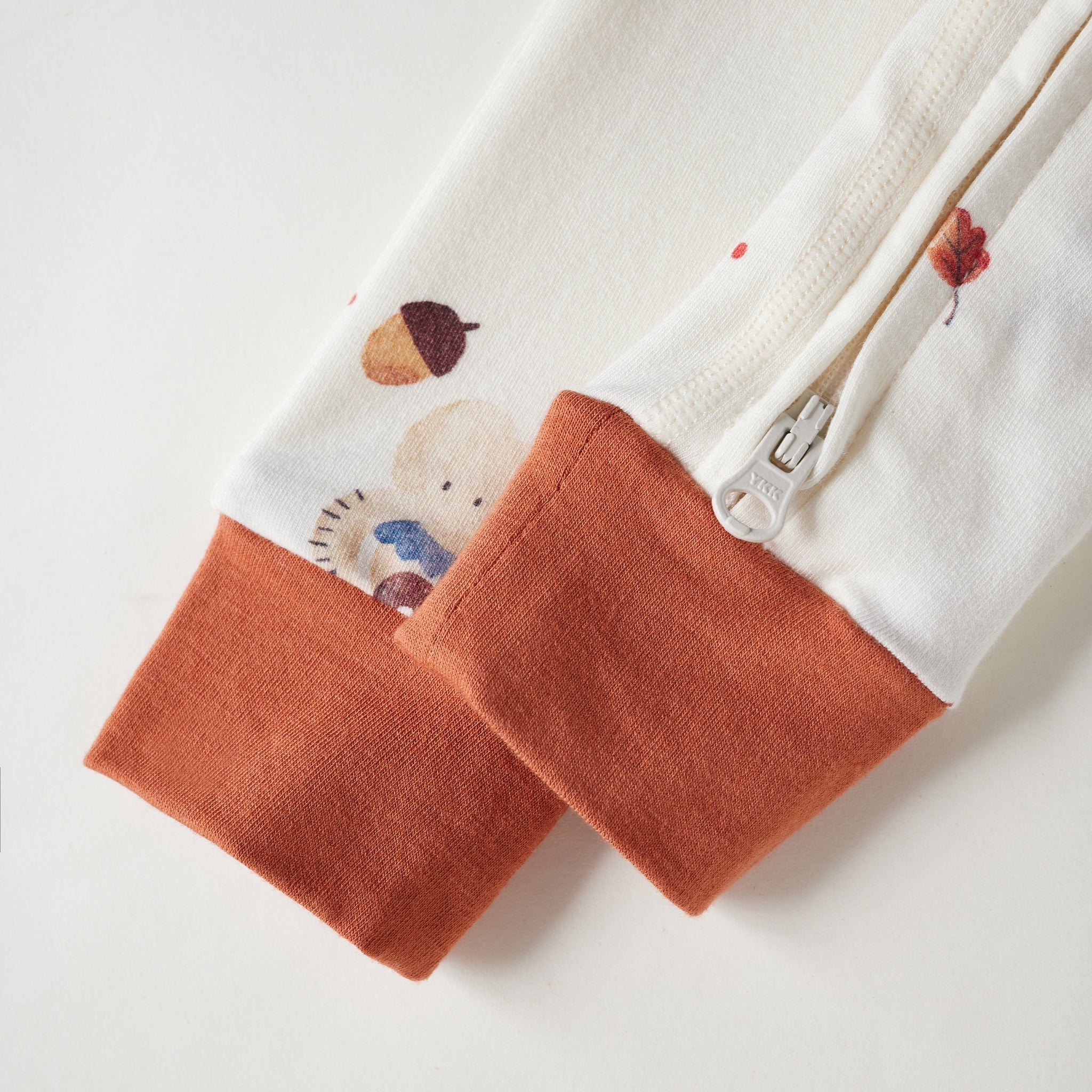 Close-up of a white zippered garment sleeve with a soft orange cuff and a small bear-and-acorn print near the cuff.