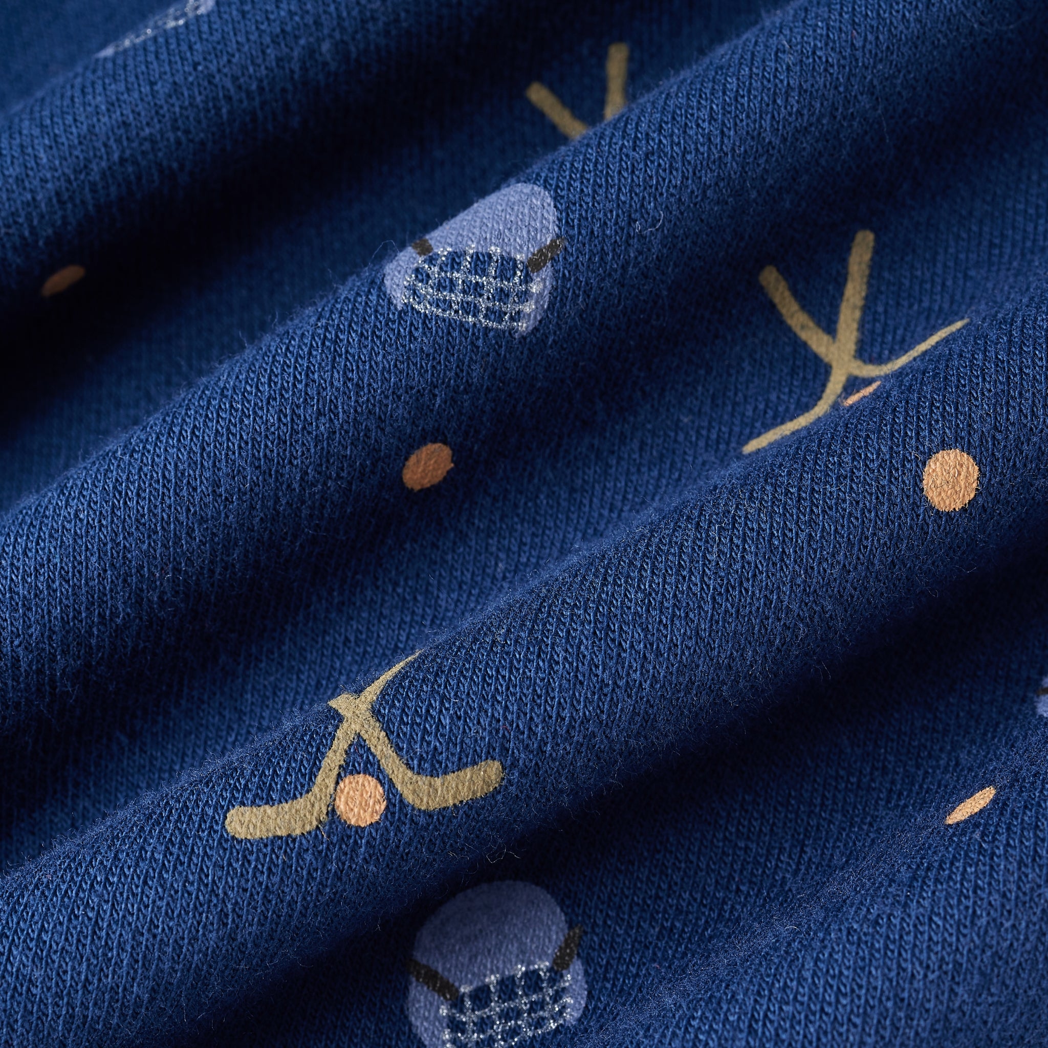 A close-up of navy blue knit fabric with a repeating pattern of small gold crescent moons, orange dots, and light blue-and-white geometric motifs.