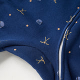 Close-up of a navy blue fabric garment with a white zipper and small gold and light blue printed motifs, including abstract shapes and a small skull-and-crossbones style design.