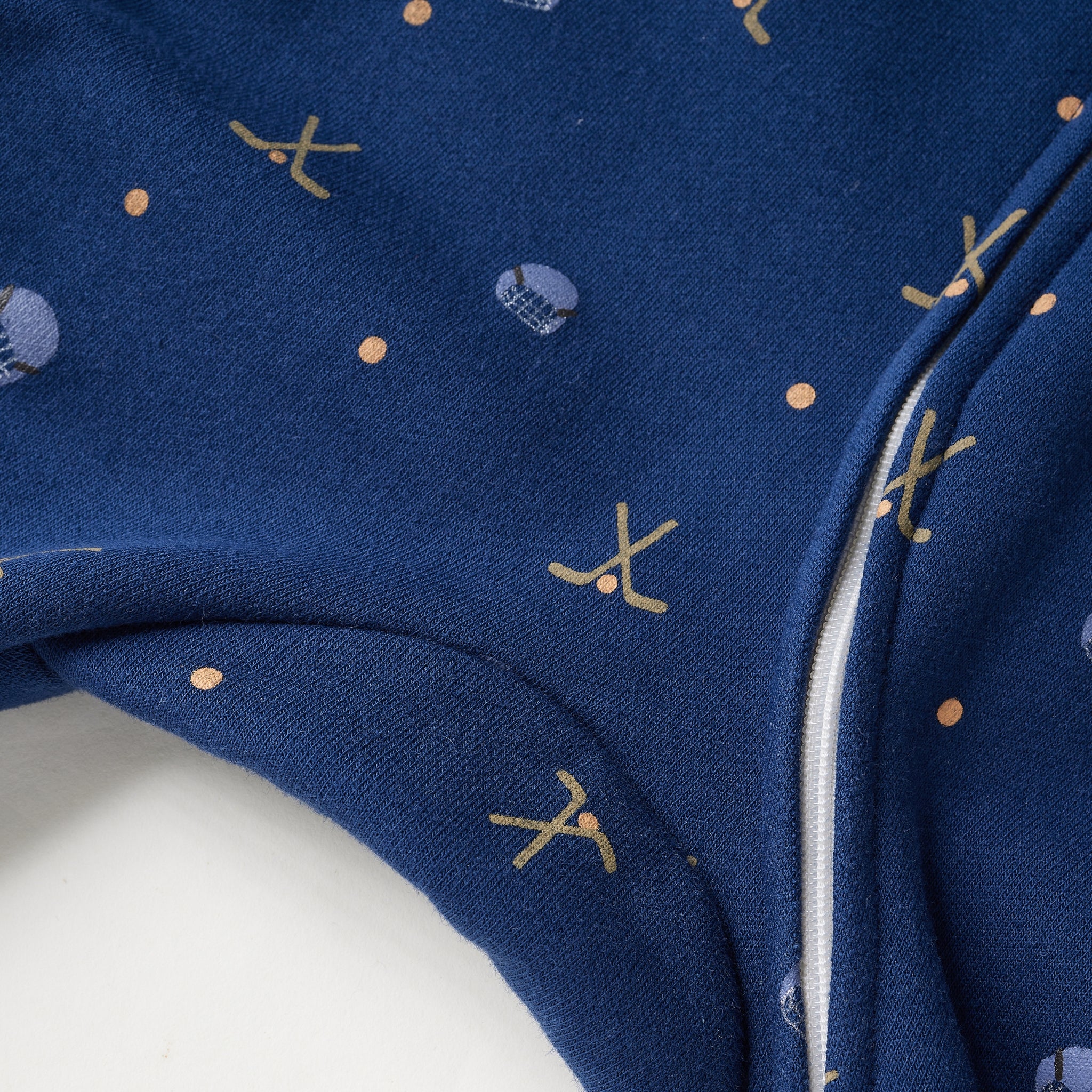 Close-up of a navy blue fabric garment with a white zipper and small gold and light blue printed motifs, including abstract shapes and a small skull-and-crossbones style design.