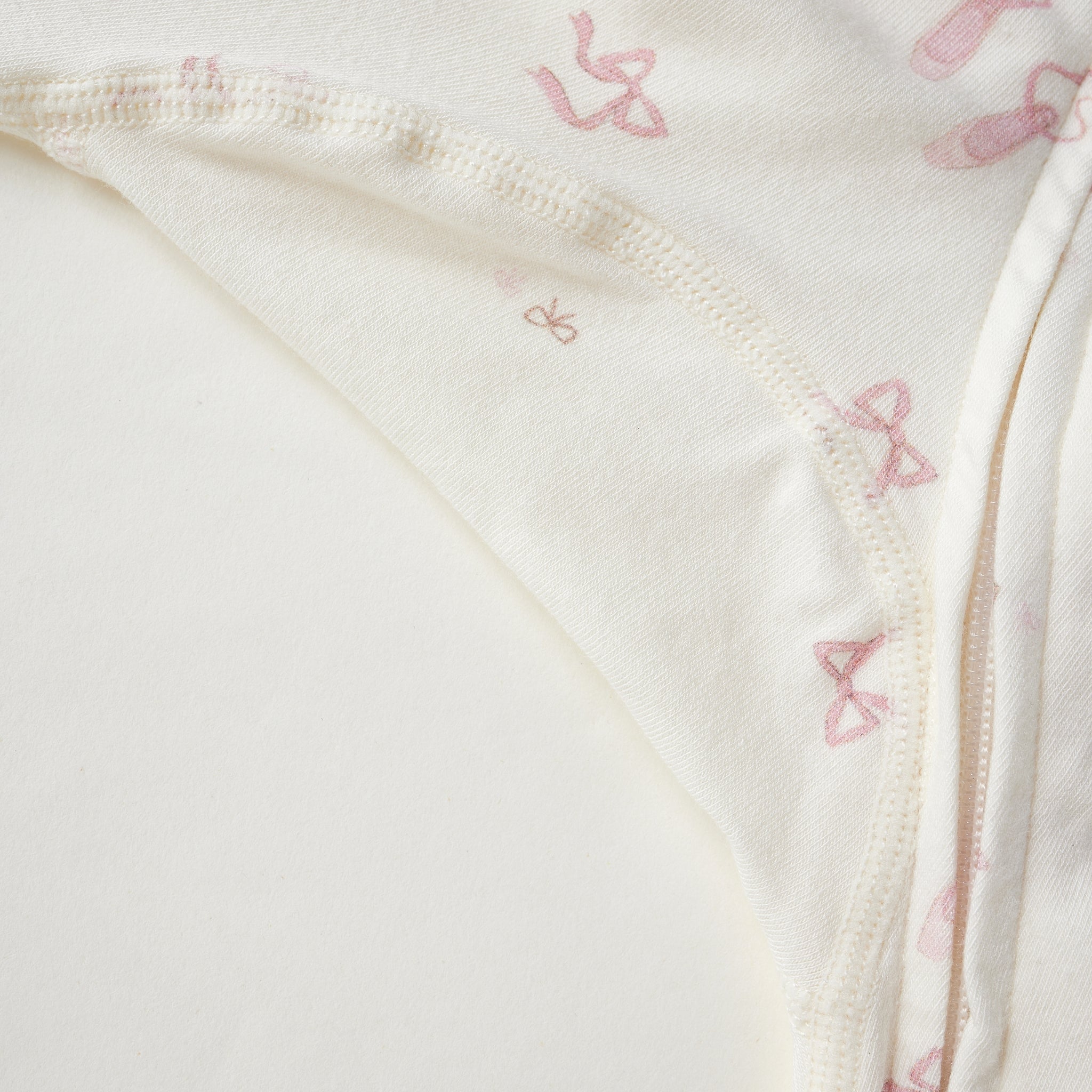 Close-up of a cream-colored fabric garment with a delicate pink bow pattern and a visible zipper.