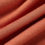A close-up of draped fabric in a warm coral or terracotta shade, showing the soft texture and fine knit detail.