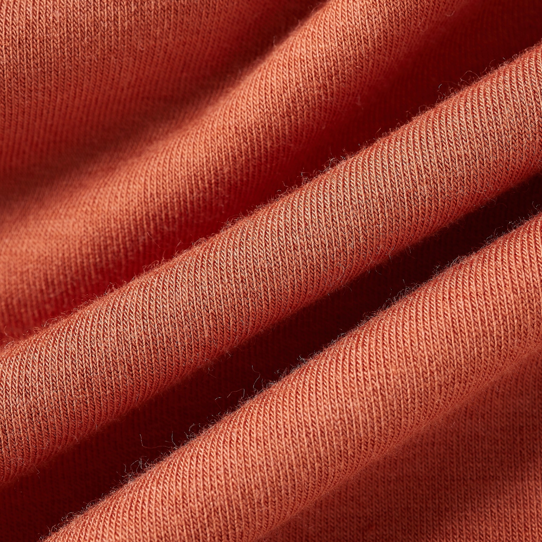 A close-up of draped fabric in a warm coral or terracotta shade, showing the soft texture and fine knit detail.