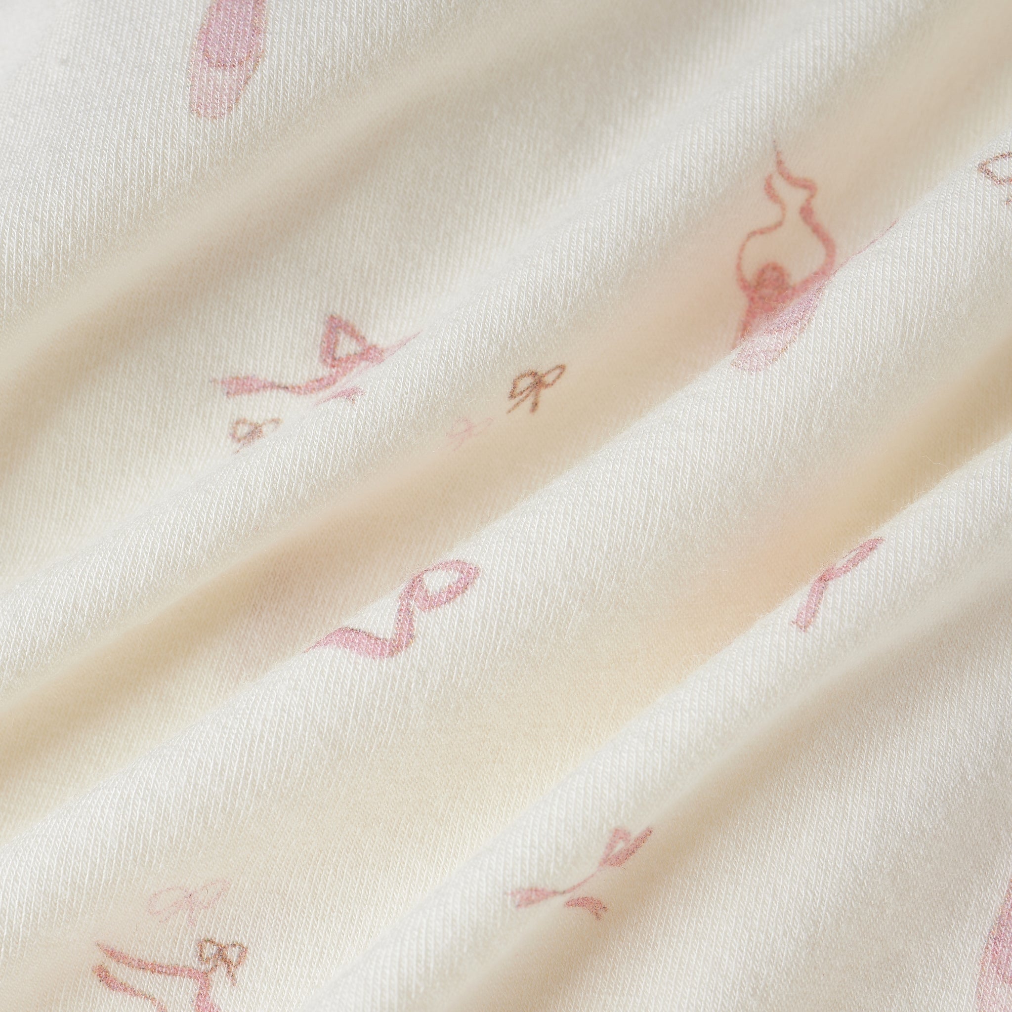 A close-up of a soft cream-colored fabric with a delicate, repeating pink ballet dancer pattern.