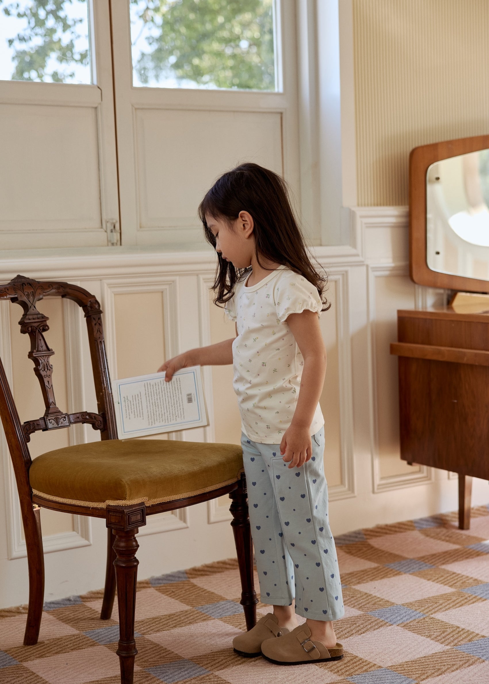 A young girl stands in front of a chair, her bright smile capturing a moment of childhood wonder and happiness