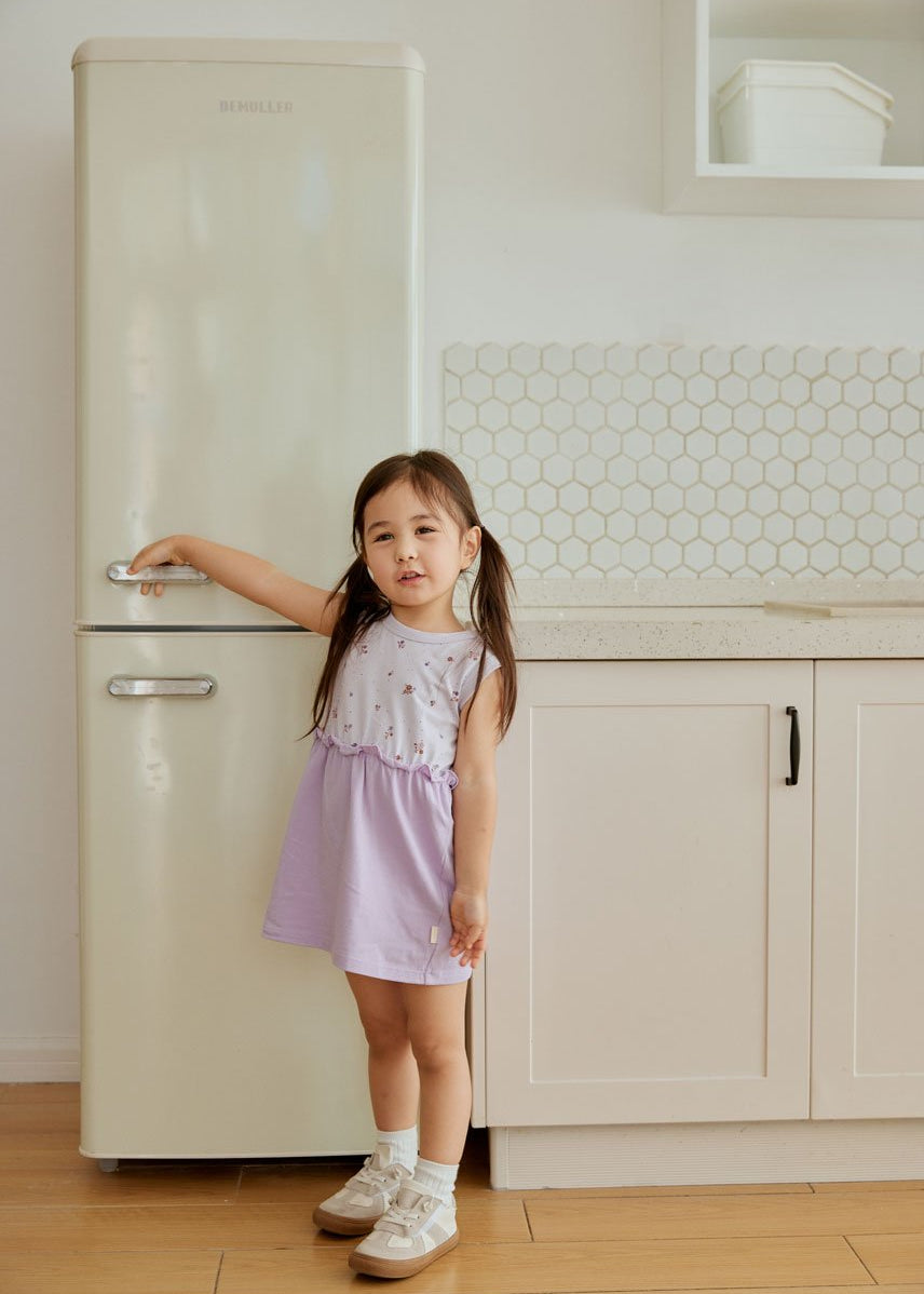 baby standing beside fridge and smiiling at you