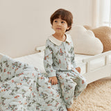 Child wearing floral pajamas sitting on a bed with a floral blanket.