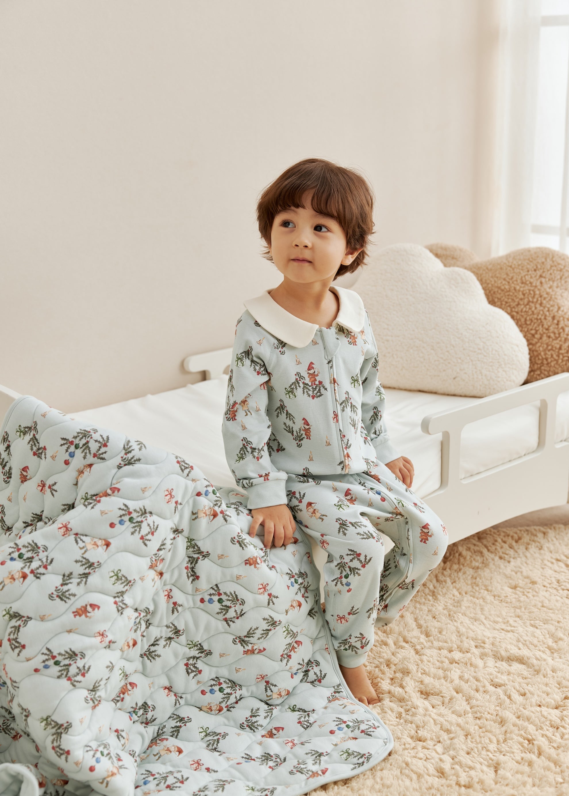 Child wearing floral pajamas sitting on a bed with a floral blanket.