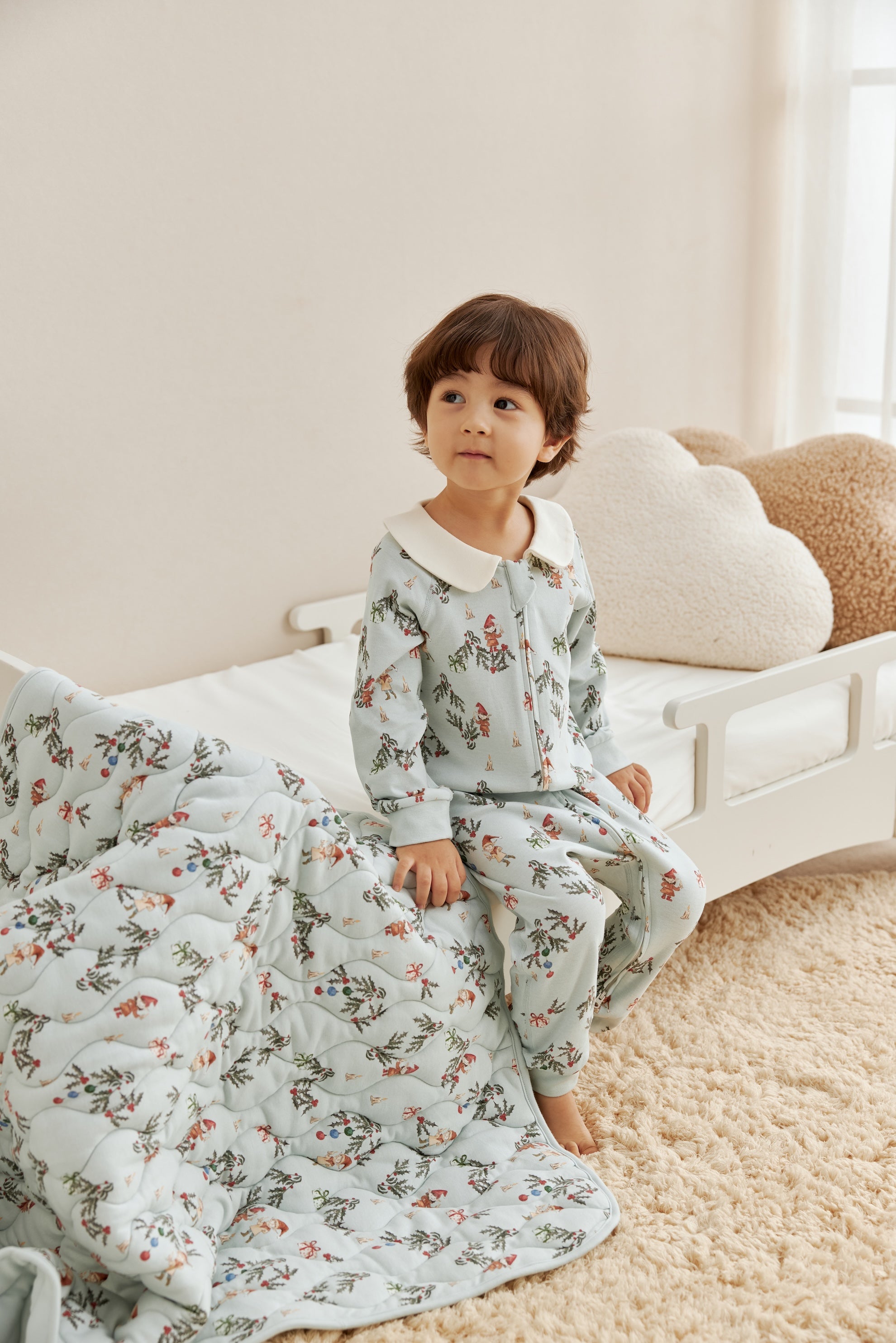 Child wearing floral pajamas sitting on a bed with a floral blanket.