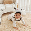 Baby in a white onesie with black accents crawling on a beige carpet.
