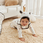 Baby in a white onesie with black accents crawling on a beige carpet.