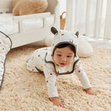 Baby in a white onesie with black accents crawling on a beige carpet.