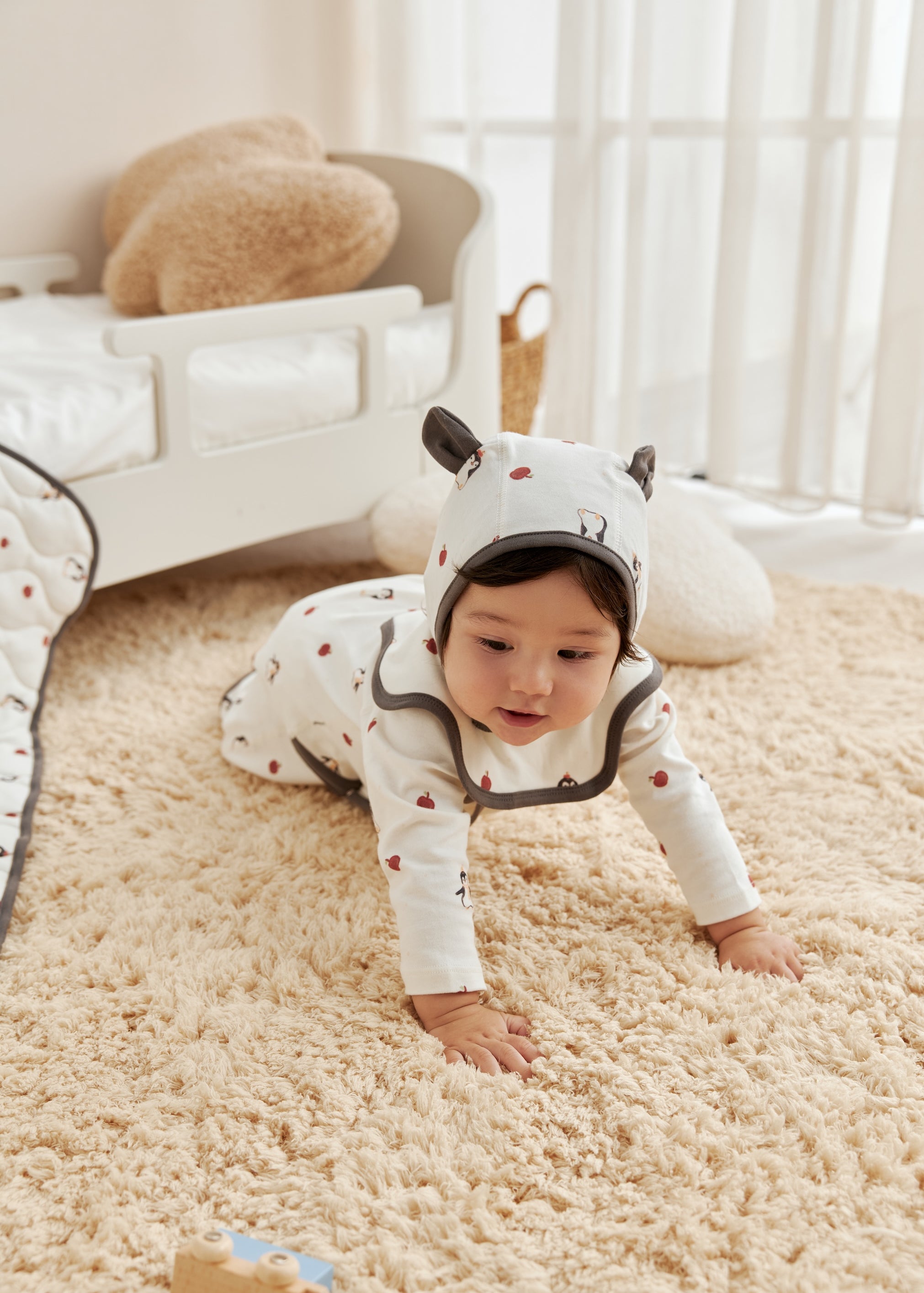 Baby in a white onesie with black accents crawling on a beige carpet.