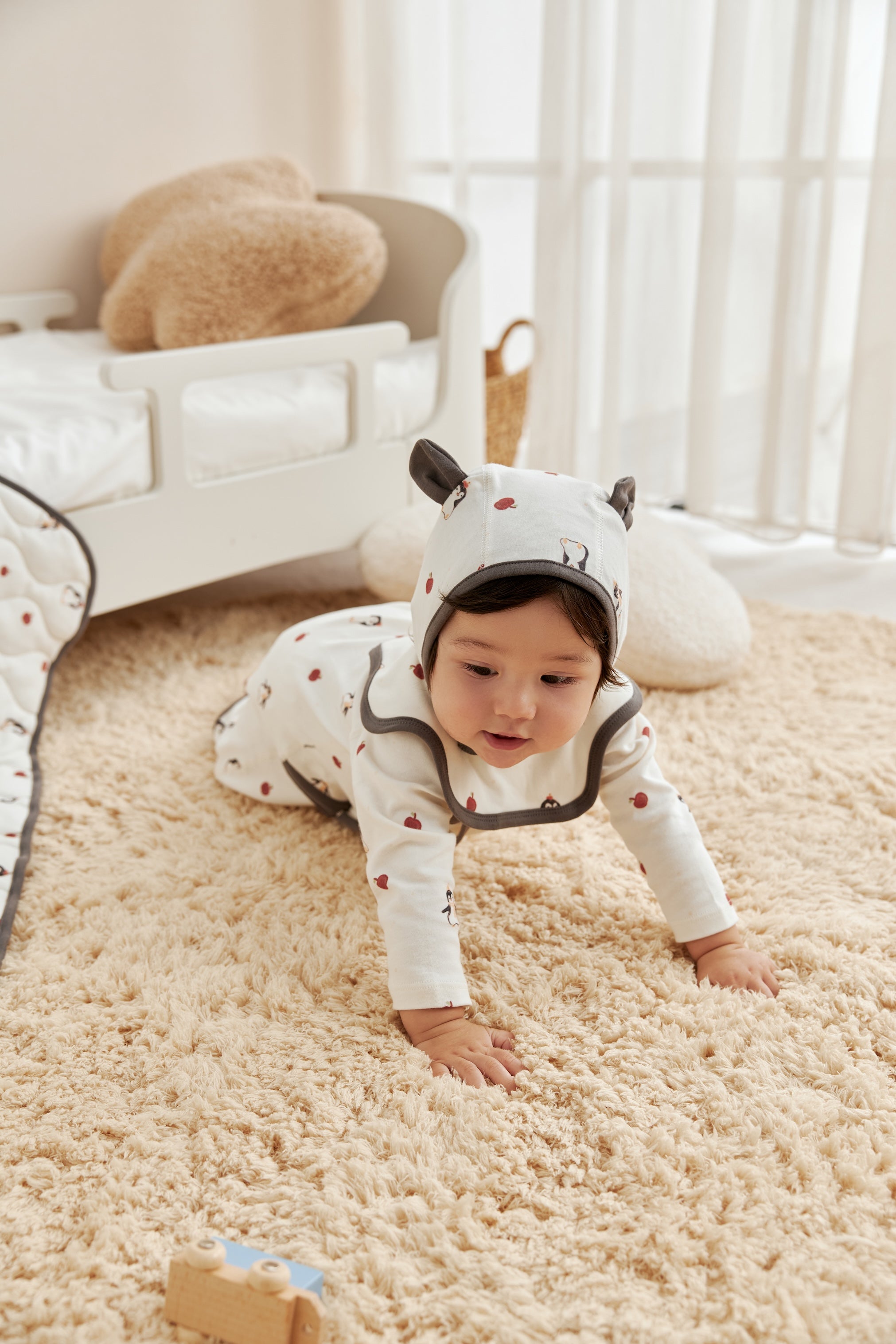 Baby in a white onesie with black accents crawling on a beige carpet.