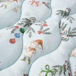 Patterned fabric with Christmas-themed designs including elves, presents, and holly leaves on a light blue background.