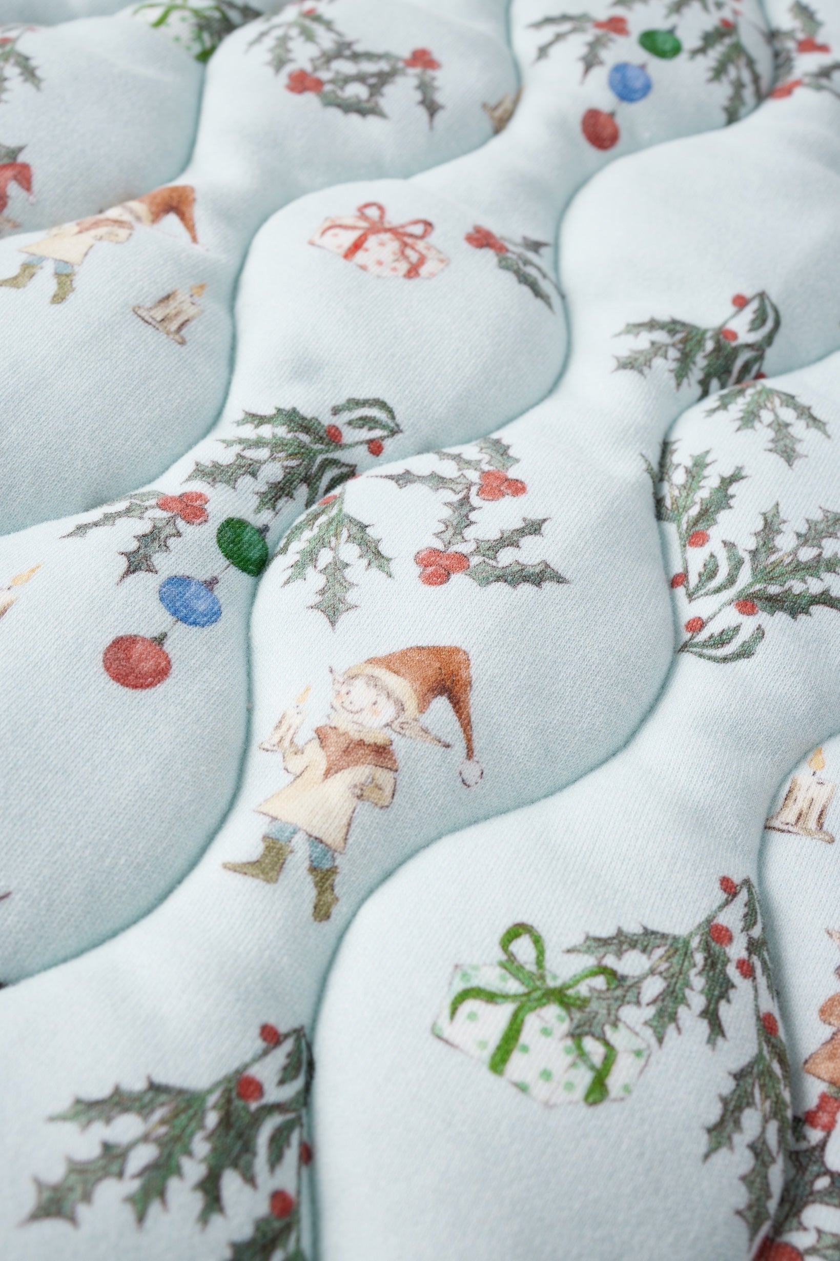 Patterned fabric with Christmas-themed designs including elves, presents, and holly leaves on a light blue background.