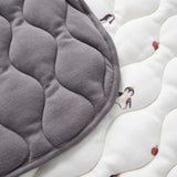 Gray quilted pad on a white surface with penguin patterns