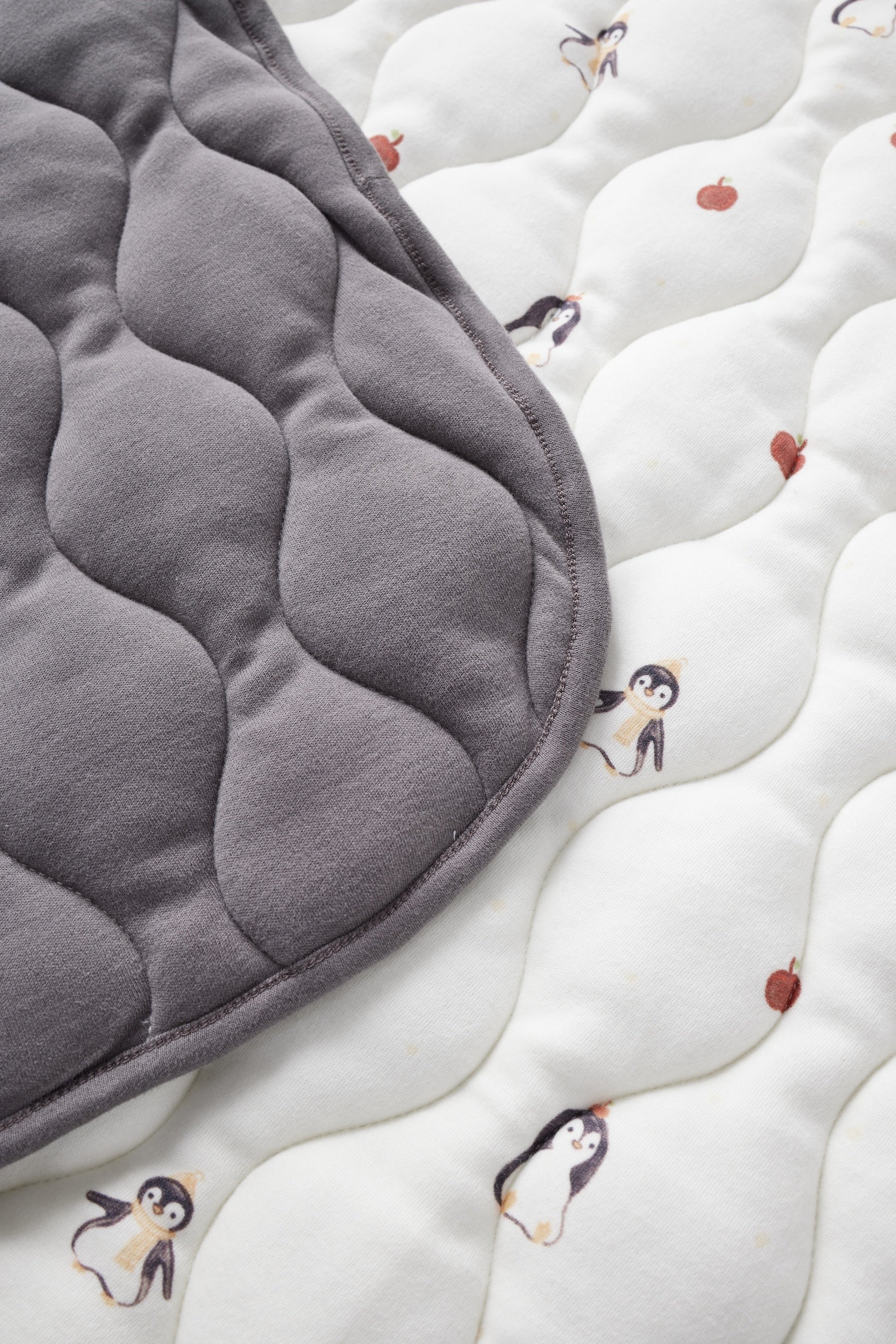 Gray quilted pad on a white surface with penguin patterns