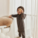 Child in a dark gray onesie holding a yellow object in a bright room with white curtains.