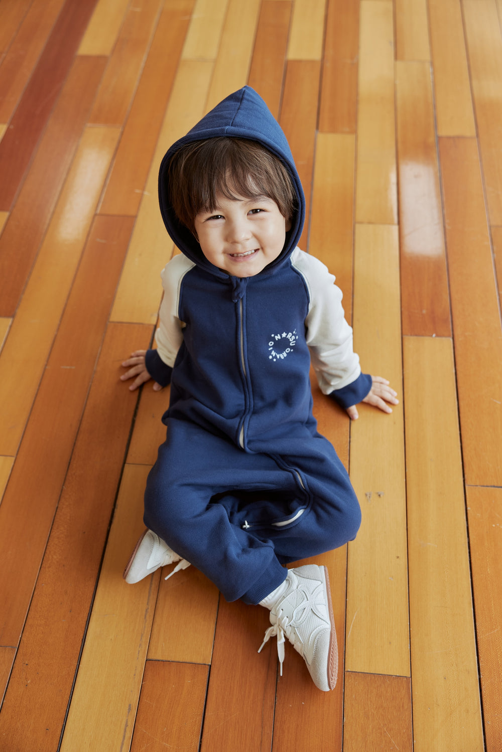 Child wearing a blue sleeper on a wooden floor