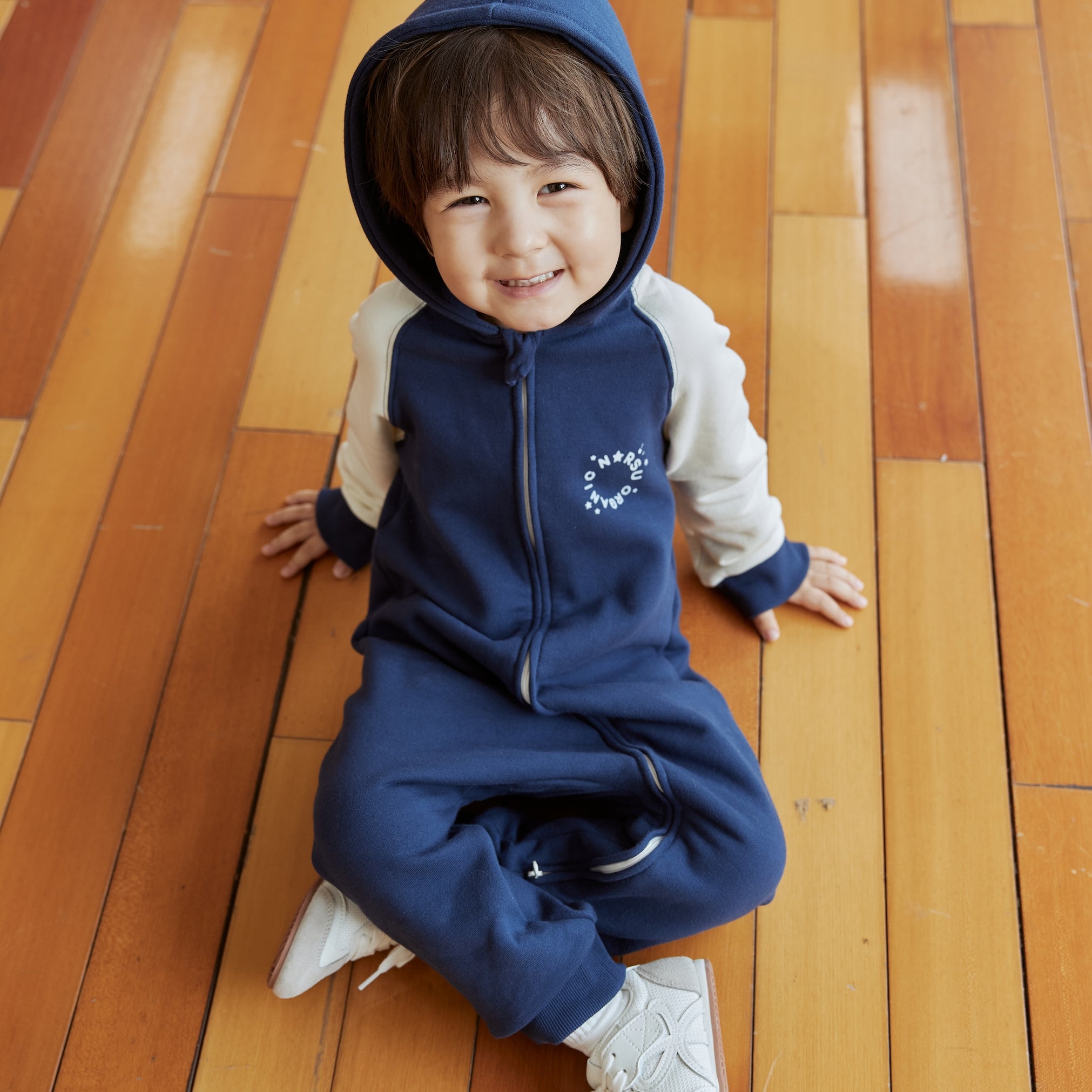Child wearing a blue sleeper on a wooden floor
