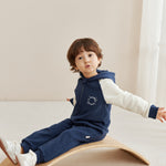Child sitting on a wooden balance board wearing a navy blue outfit with norsu logo.