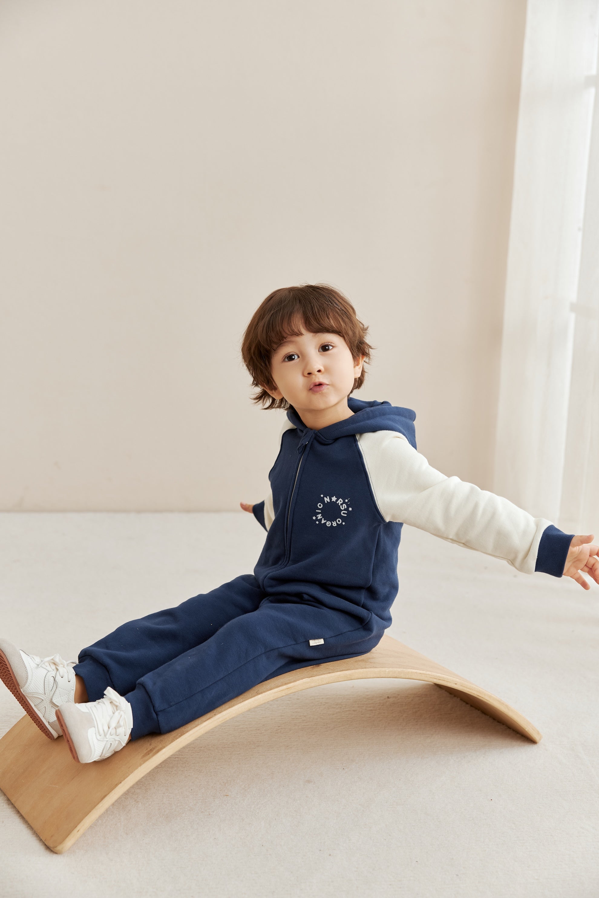 Child sitting on a wooden balance board wearing a navy blue outfit with norsu logo.