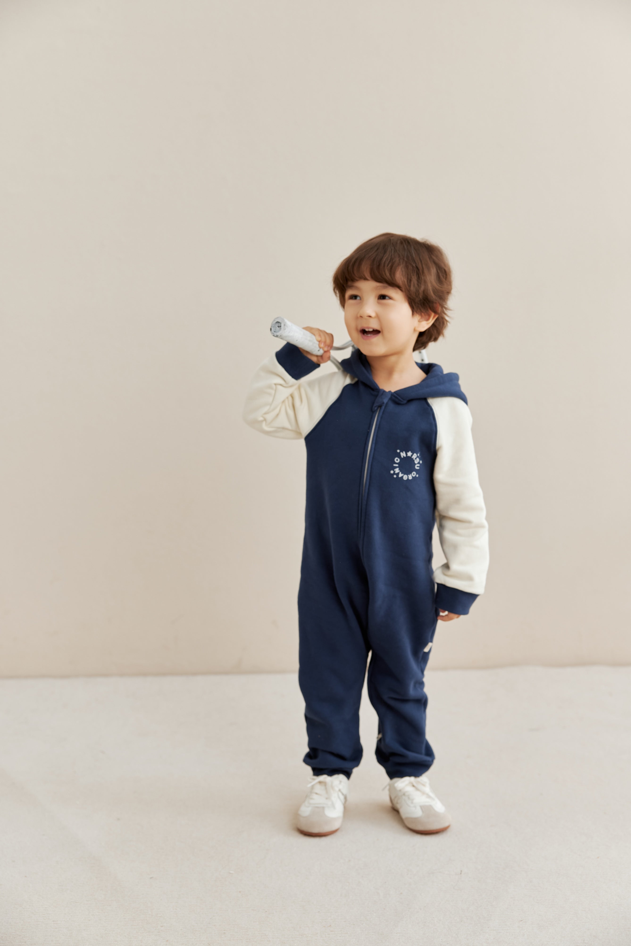 Child wearing a navy and white sleeper with a hood on a beige background